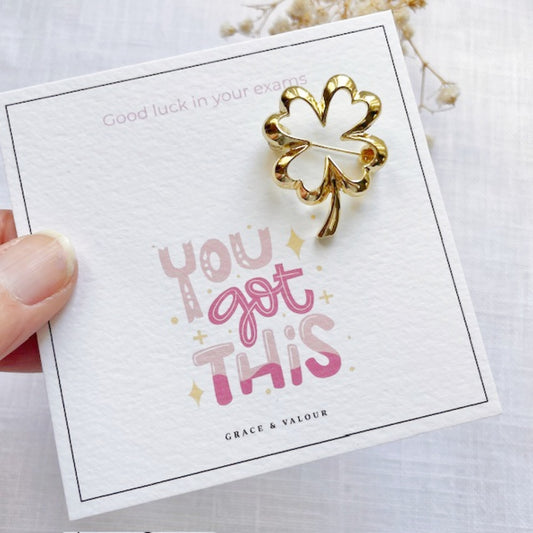 Gold four-leaf clover brooch on a card with 'You got this' text, held by a hand.