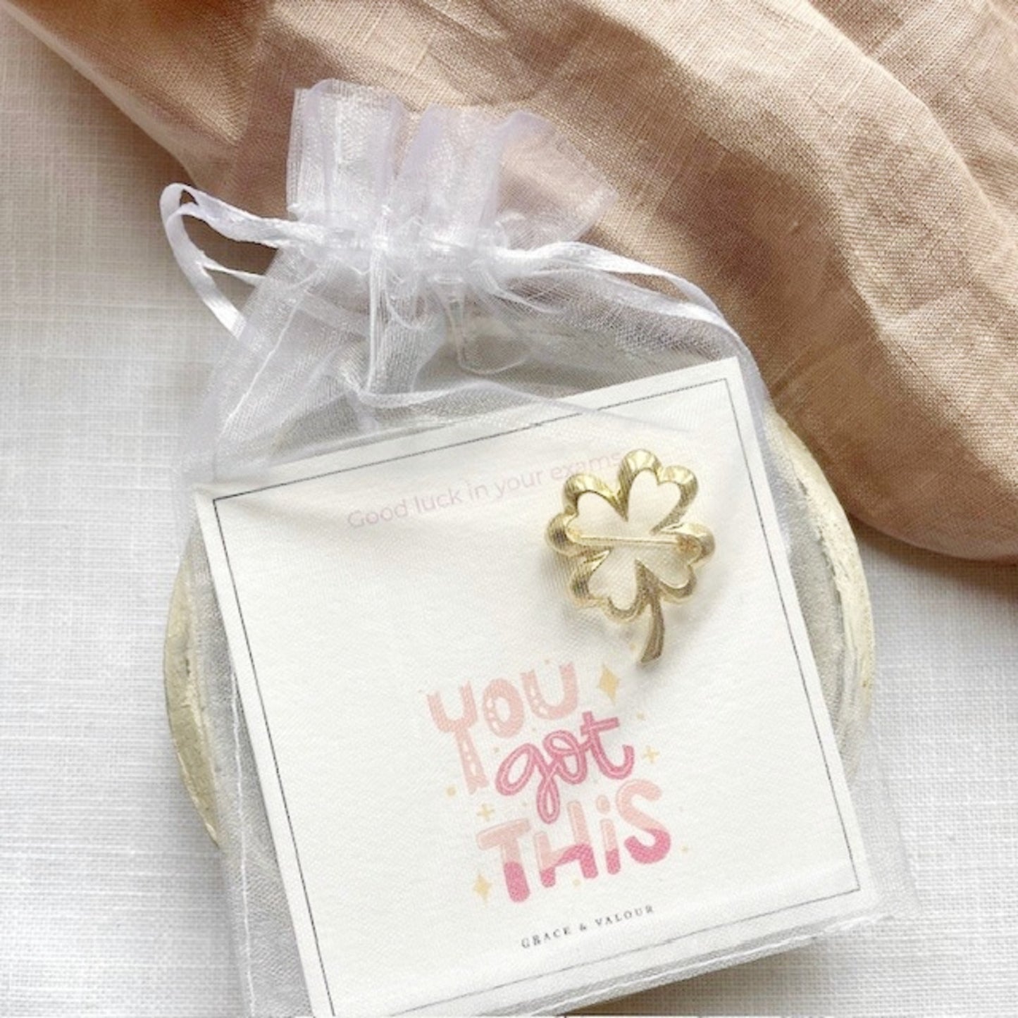 Gold four-leaf clover brooch on a card with 'You got this' text, wrapped in a sheer chiffon pouch ready for gifting.