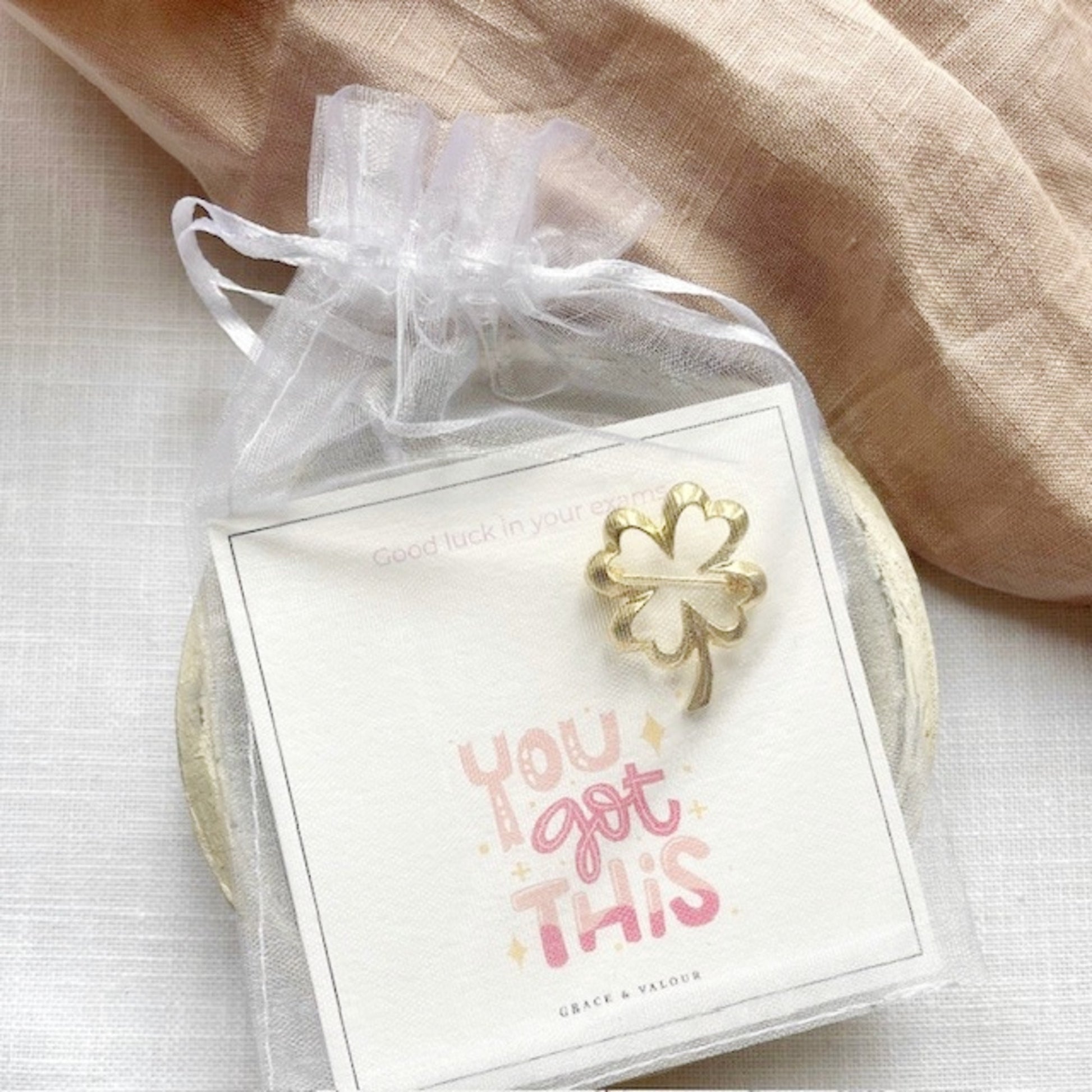 Gold four-leaf clover brooch on a card with 'You got this' text, wrapped in a sheer chiffon pouch ready for gifting.