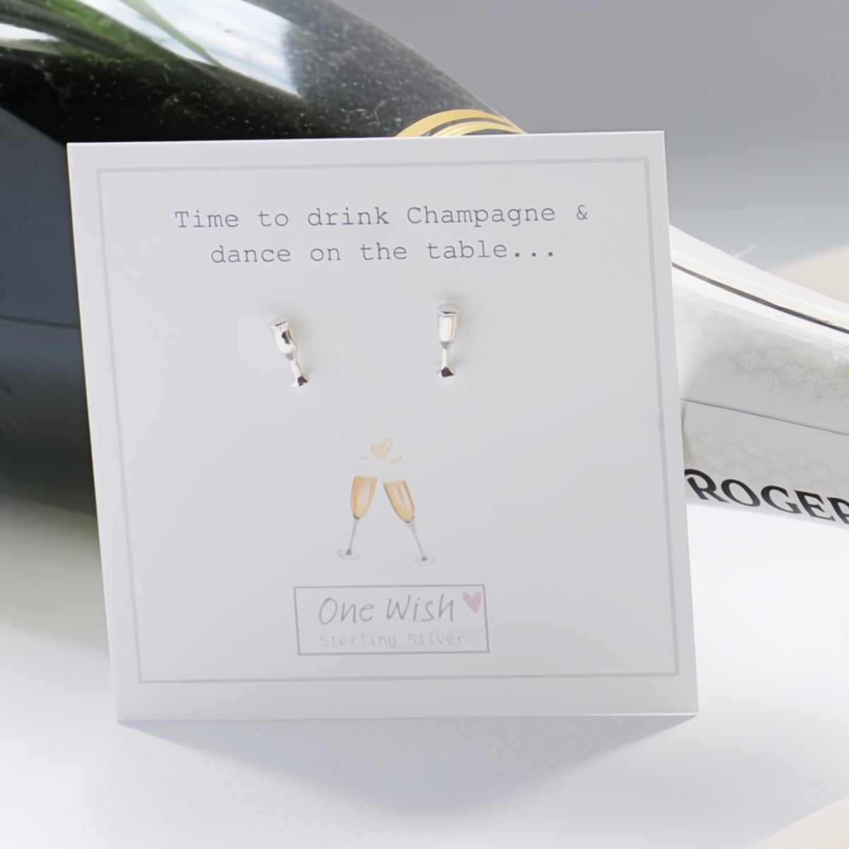 A pair of small silver stud earrings displayed on a white card that reads 'Time to drink Champagne & dance on the table.