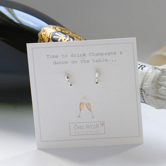 A pair of small silver stud earrings displayed on a white card that reads 'Time to drink Champagne & dance on the table.