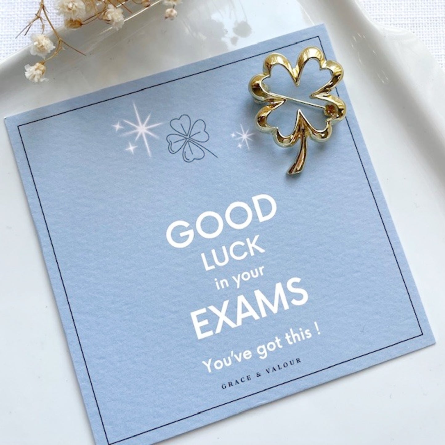 Good luck card with gold lucky clover brooch on a light blue background