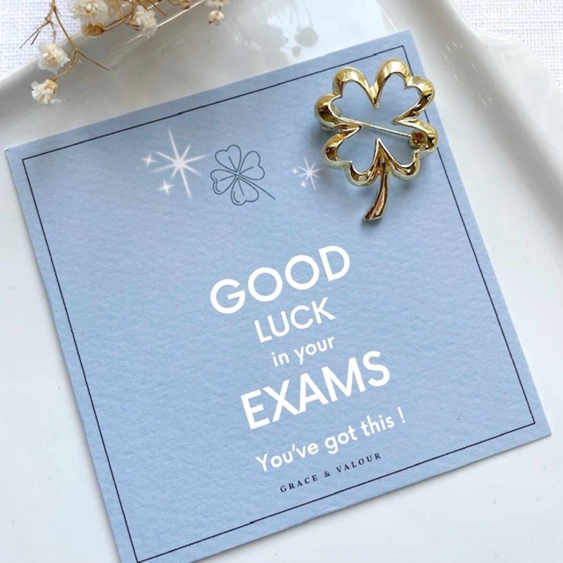Good luck card with gold lucky clover brooch on a light blue background