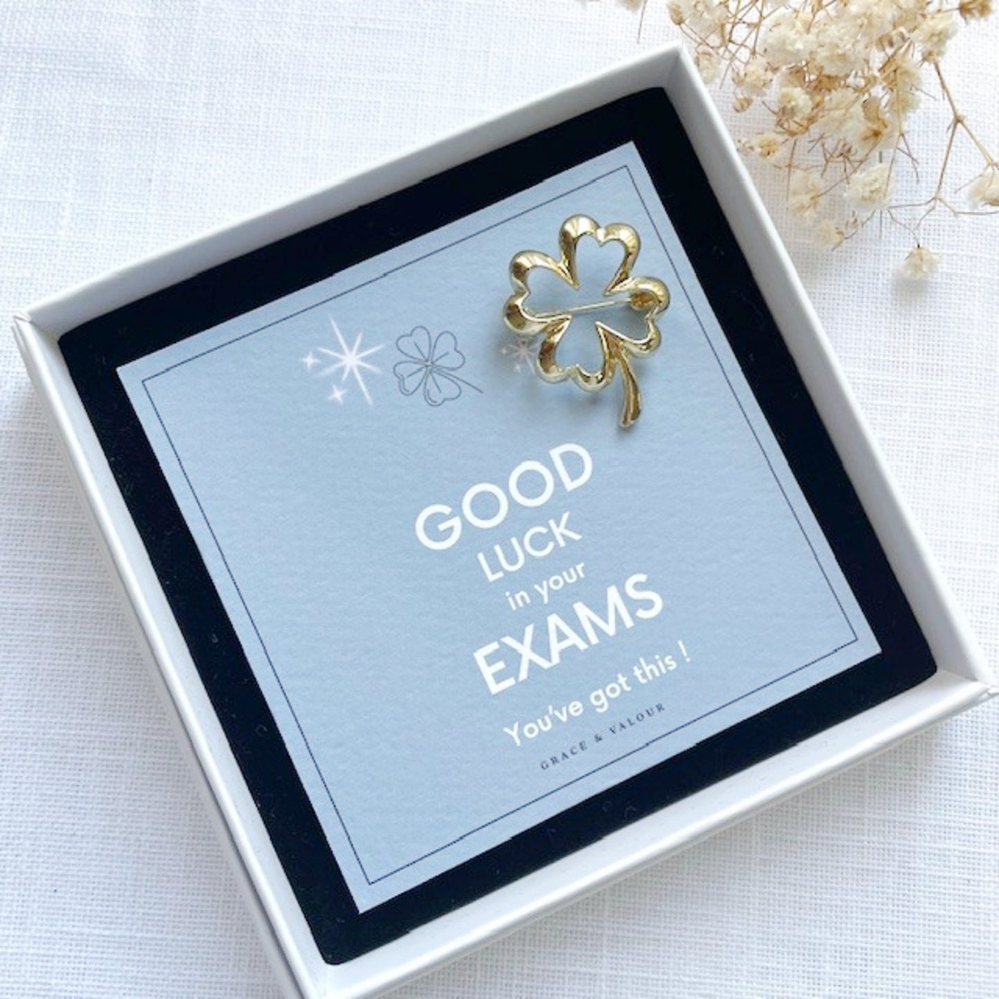 Gold four-leaf clover charm in a gift box with 'Good Luck in your Exams' message.