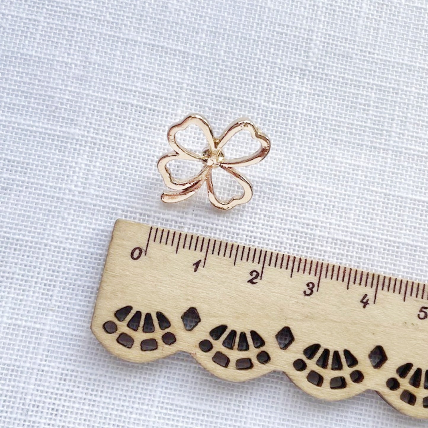 Gold four-leaf clover charm on a white background with a wooden ruler for scale.