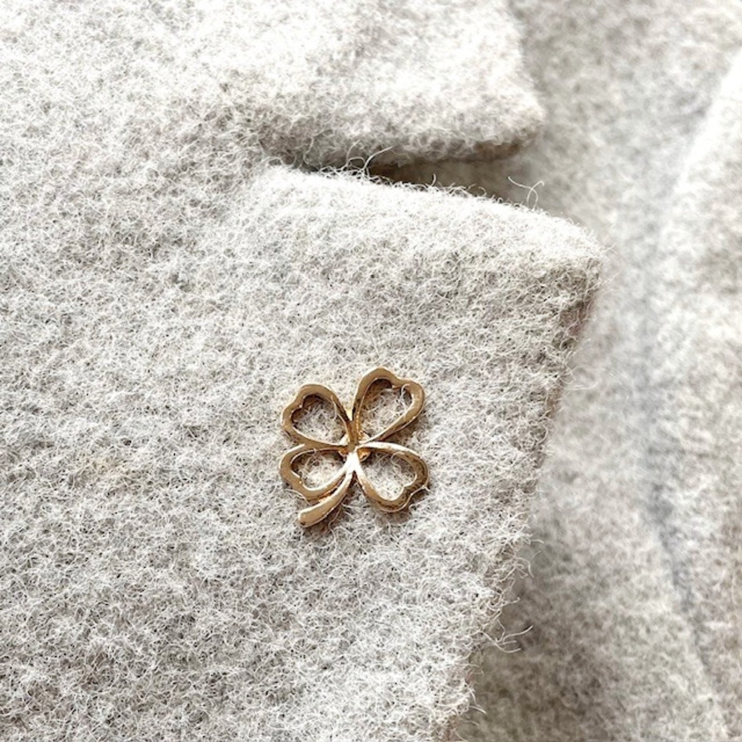 Gold four-leaf clover charm on a textured gray jacket lapel background