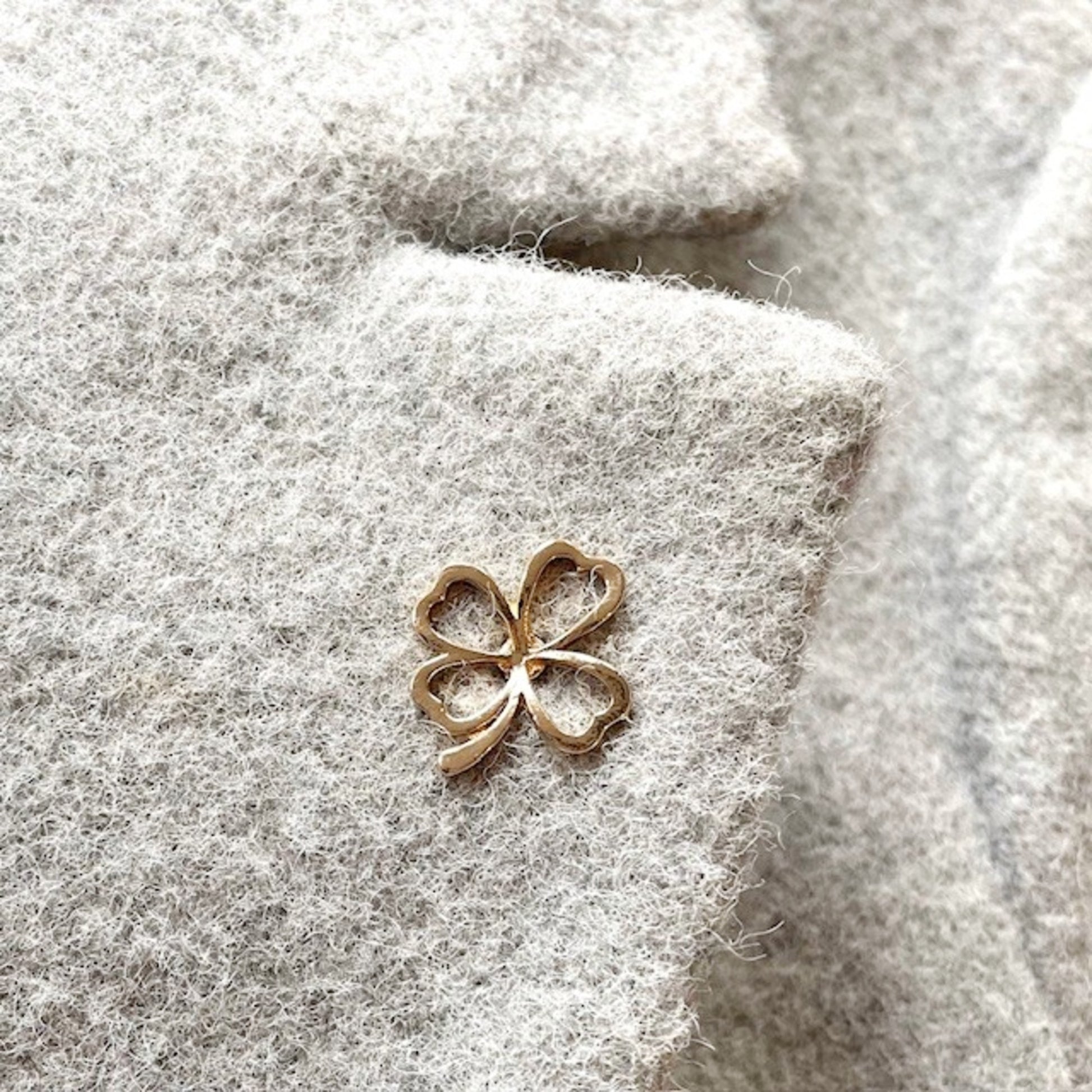 Gold four-leaf clover charm on a textured gray jacket lapel background