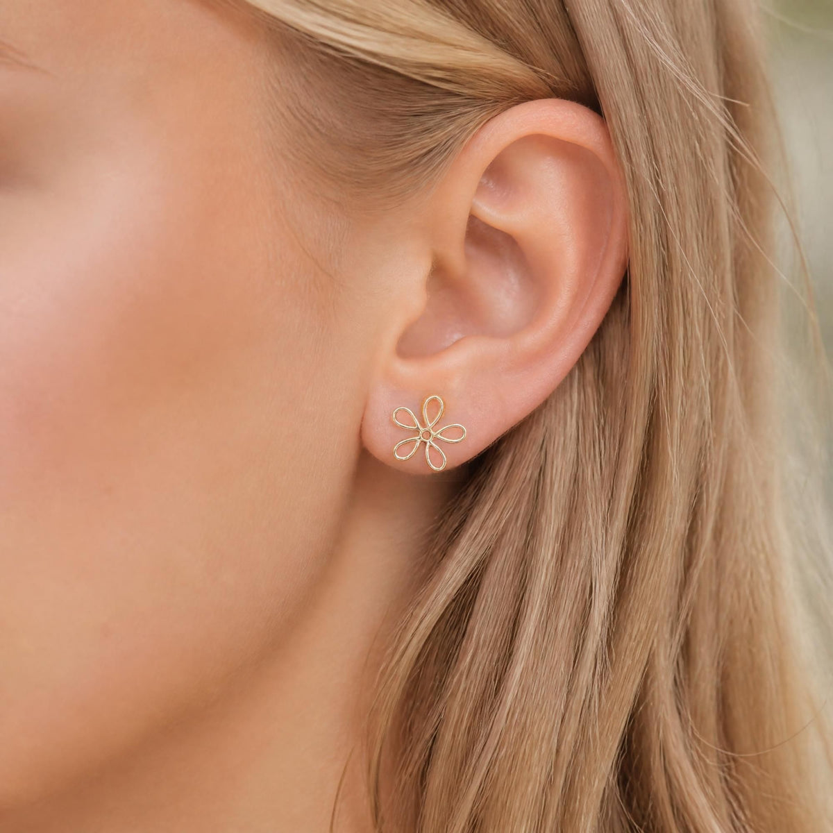 A close-up of a woman's ear wearing a small silver flower-shaped stud earring.