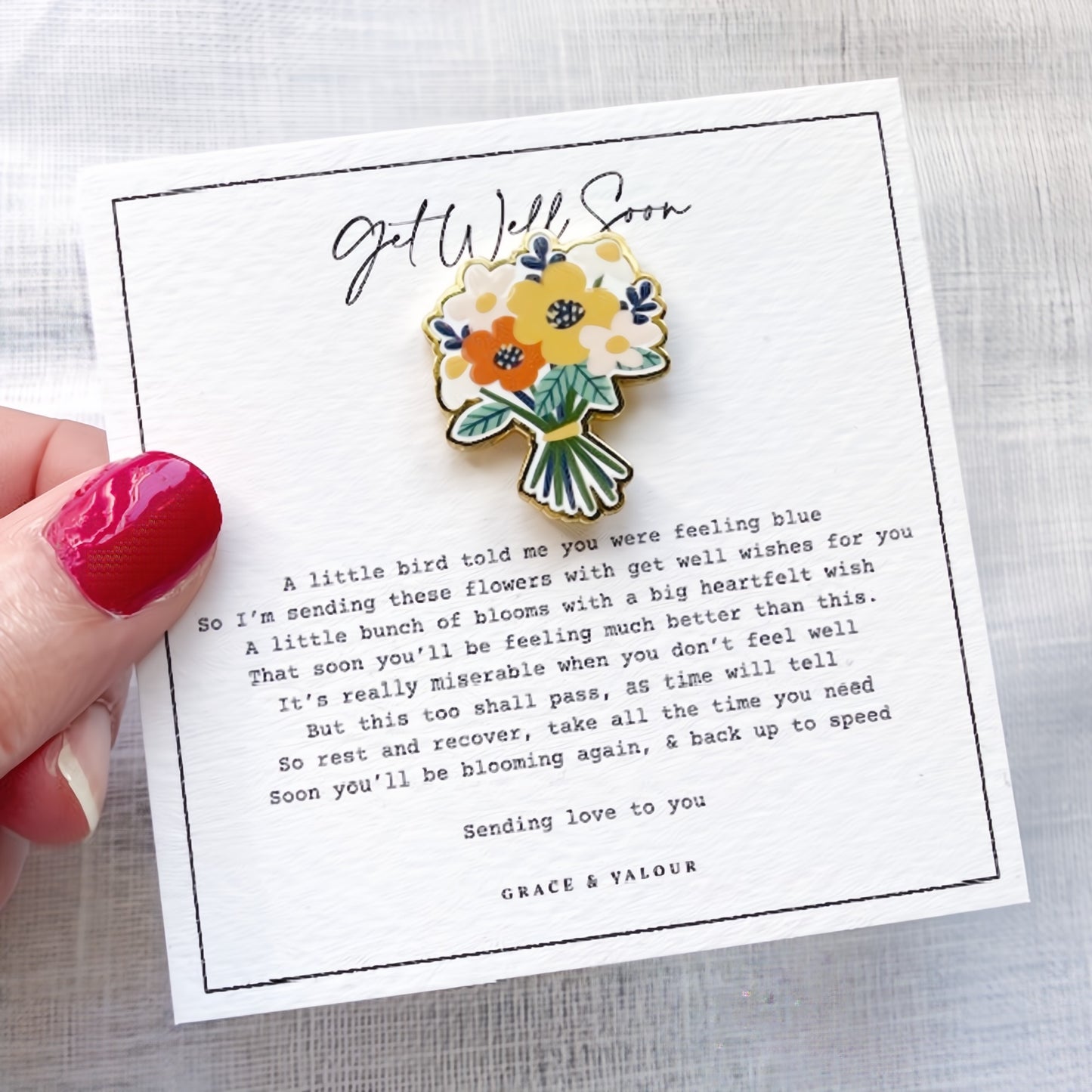 Floral brooch on a 'Get Well Soon' card held by a hand with red nail polish.