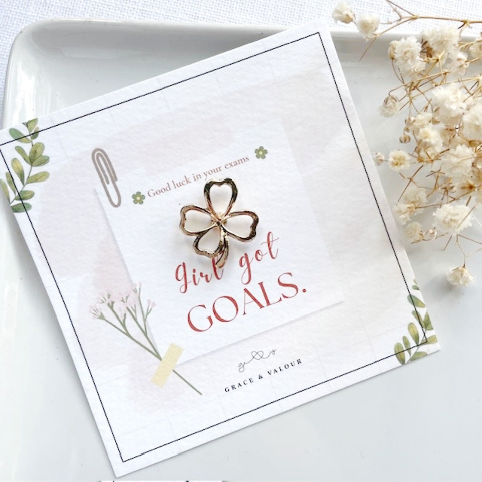 Butterfly-shaped brooch on a card with motivational text, surrounded by white flowers.