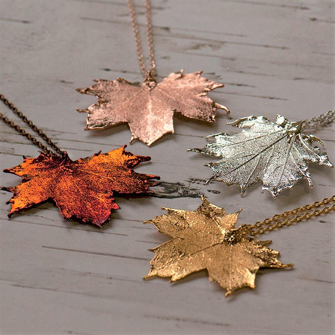 four striking metallic maple leaf necklaces on a wooden background