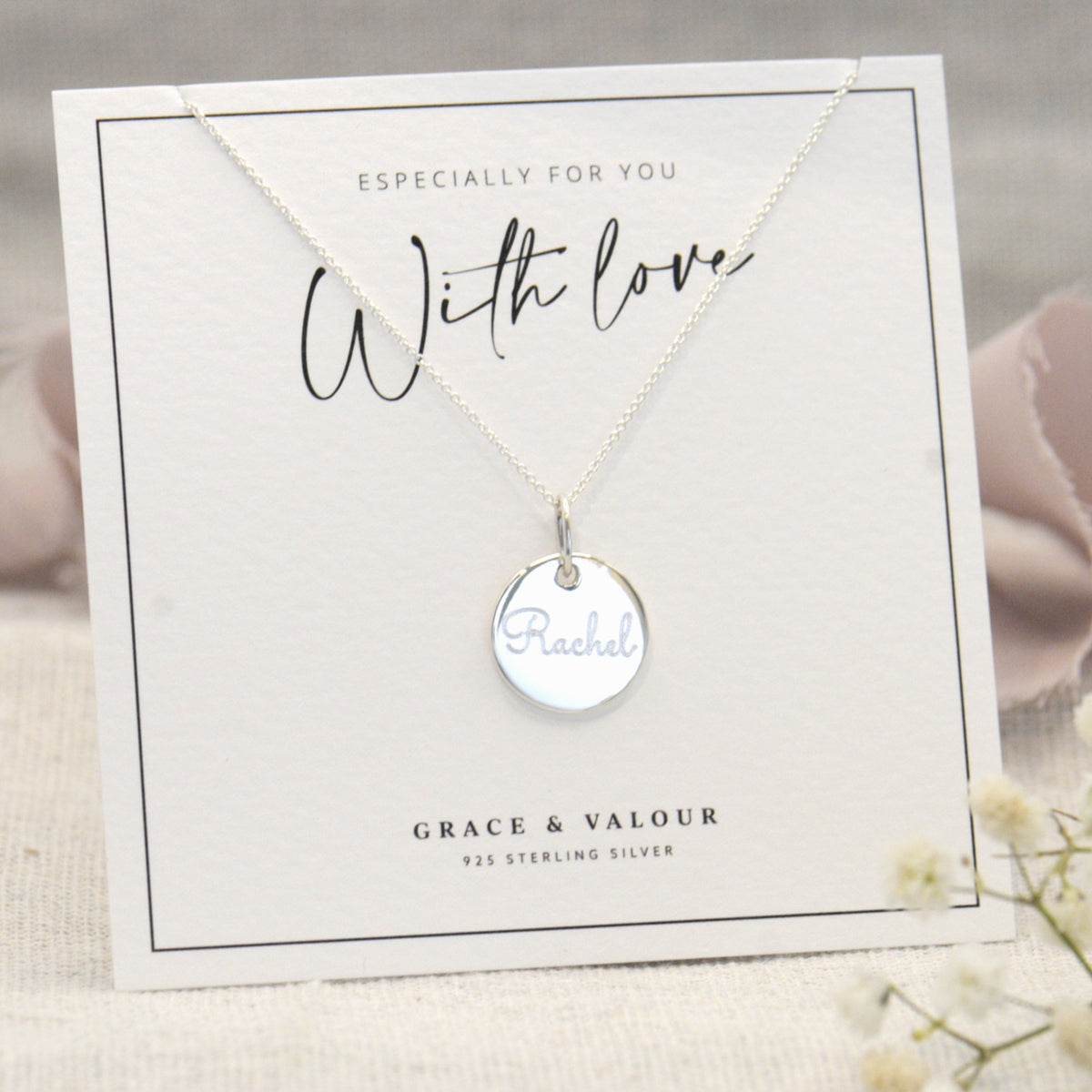 A sterling silver round disc pendant necklace with the name 'Rachel' engraved, displayed on a white gift card that reads 'With love' and 'Grace & Valour'.