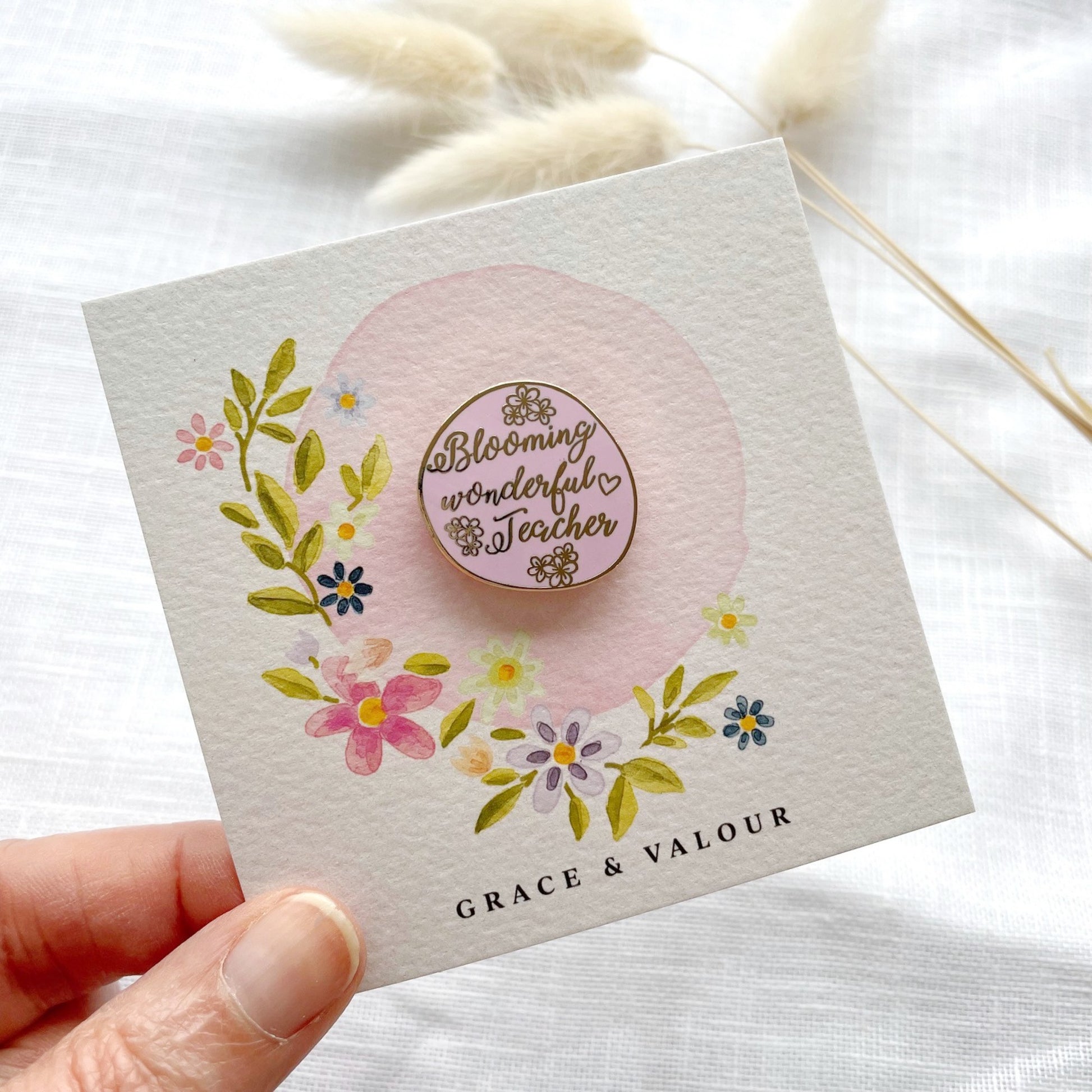 Floral-themed card with 'Blooming Wonderful Teacher' badge held by a hand on a white background.