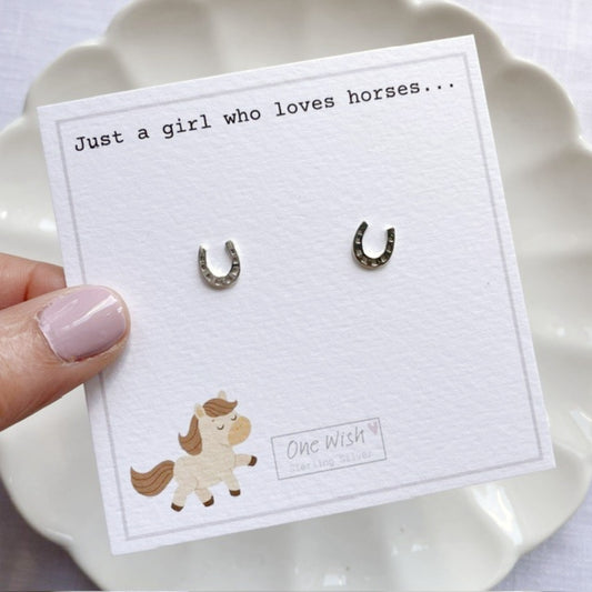 Horseshoe earrings on a card with 'Just a girl who loves horses' text, held by a hand.