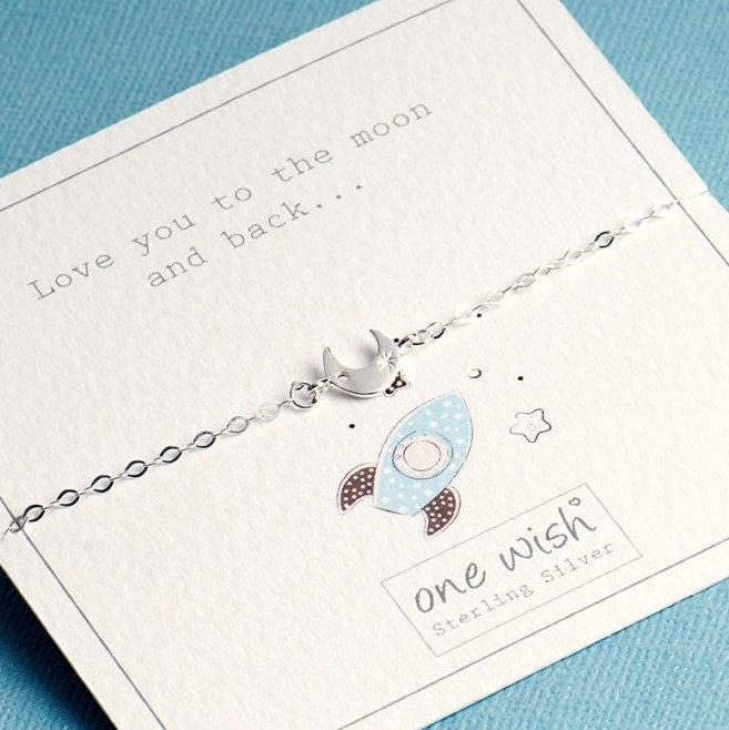 A delicate sterling silver bracelet with a crescent moon charm, displayed on its white gift card which reads 'Love you to the moon and back.