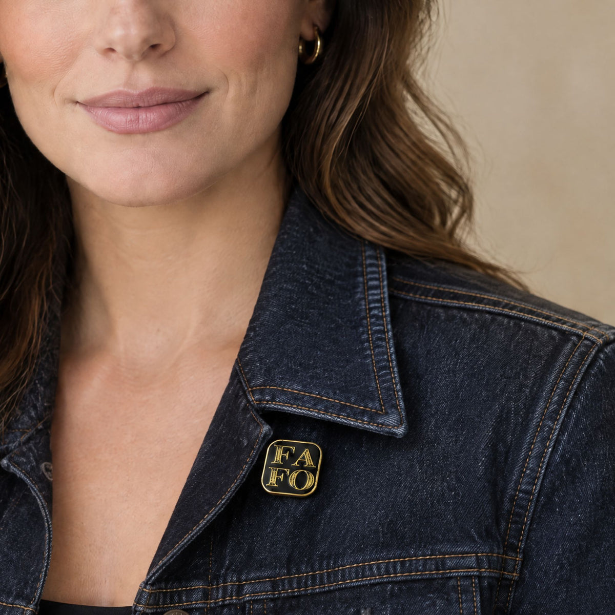 brunette model wearing the square FAFO black and gold enamel pin on her dark denim jacket