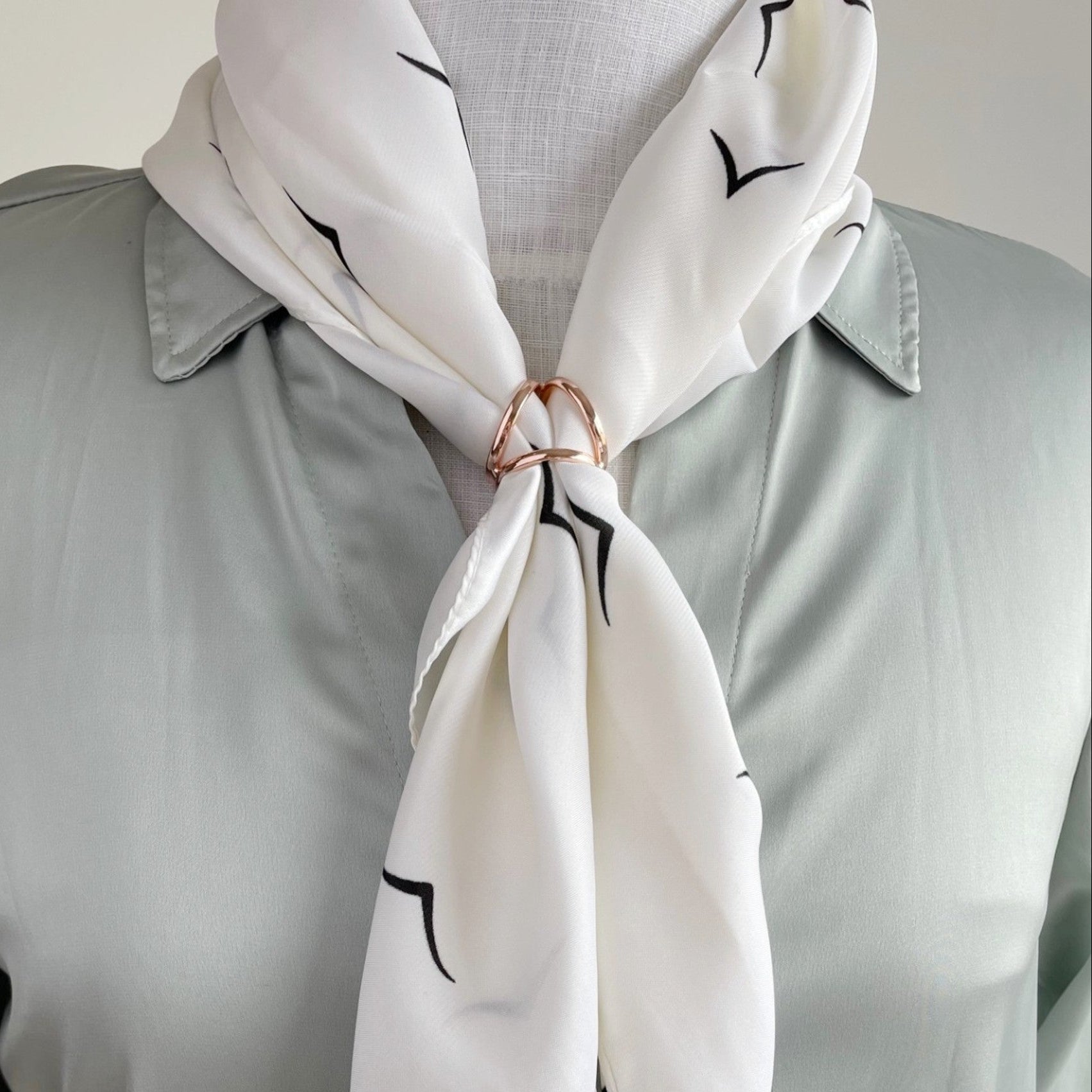 White scarf with black patterns worn over a light gray shirt showing the triple scarf ring being worn