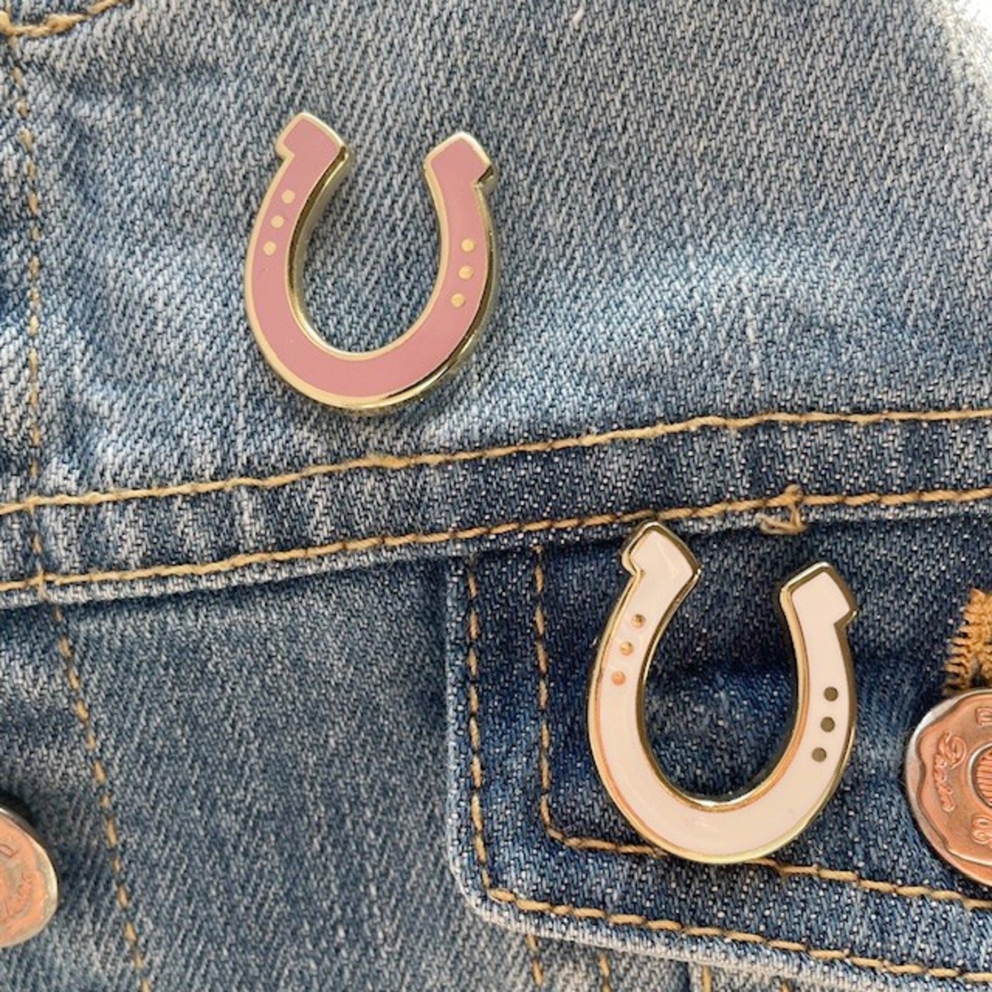 Pink and gold horseshoe pins on a denim jacket