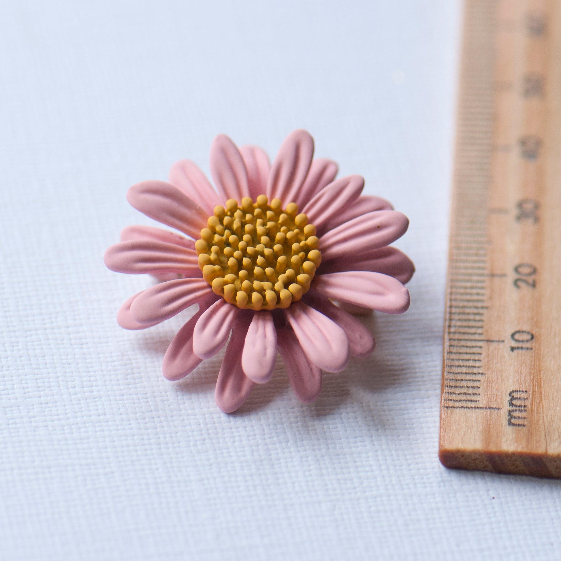 Pink daisy flower brooch next to a wooden ruler for scale.