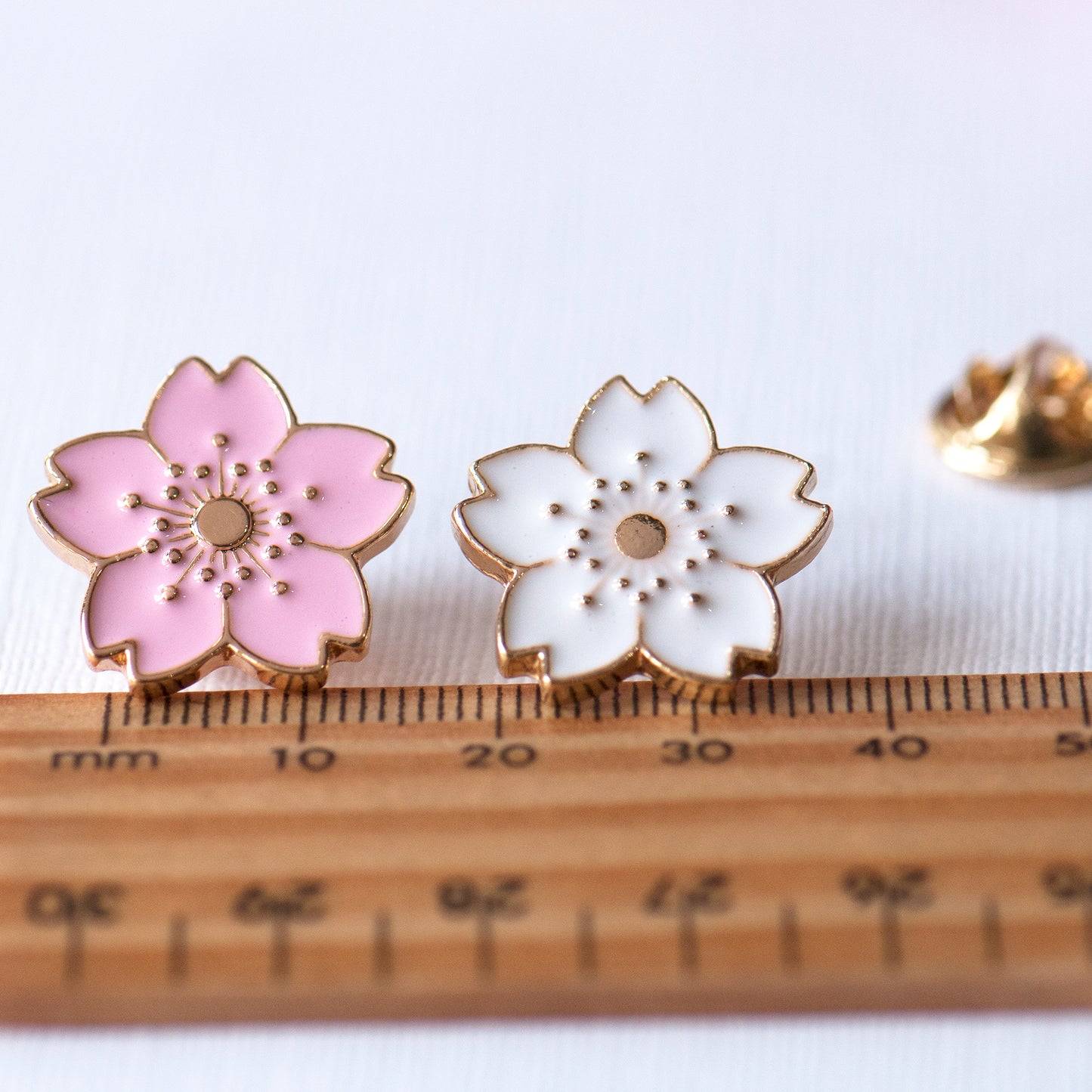 Pink and white cherry blossom enamel pins with a ruler showing the scale