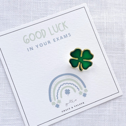 Four-leaf clover pin on a card with 'Good Luck in Your Exams' text and rainbow design.
