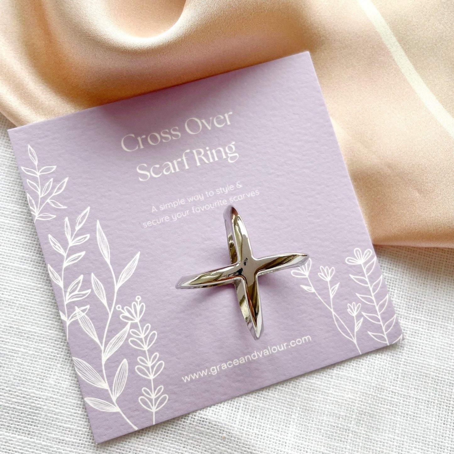 Silver scarf ring on a purple card with decorative elements, placed on a soft fabric background.