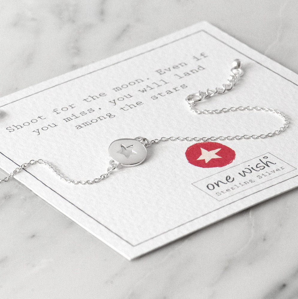 A silver bracelet with a star-shaped cutout in the center, displayed on a white card with an inspirational quote by Oscar Wilde.