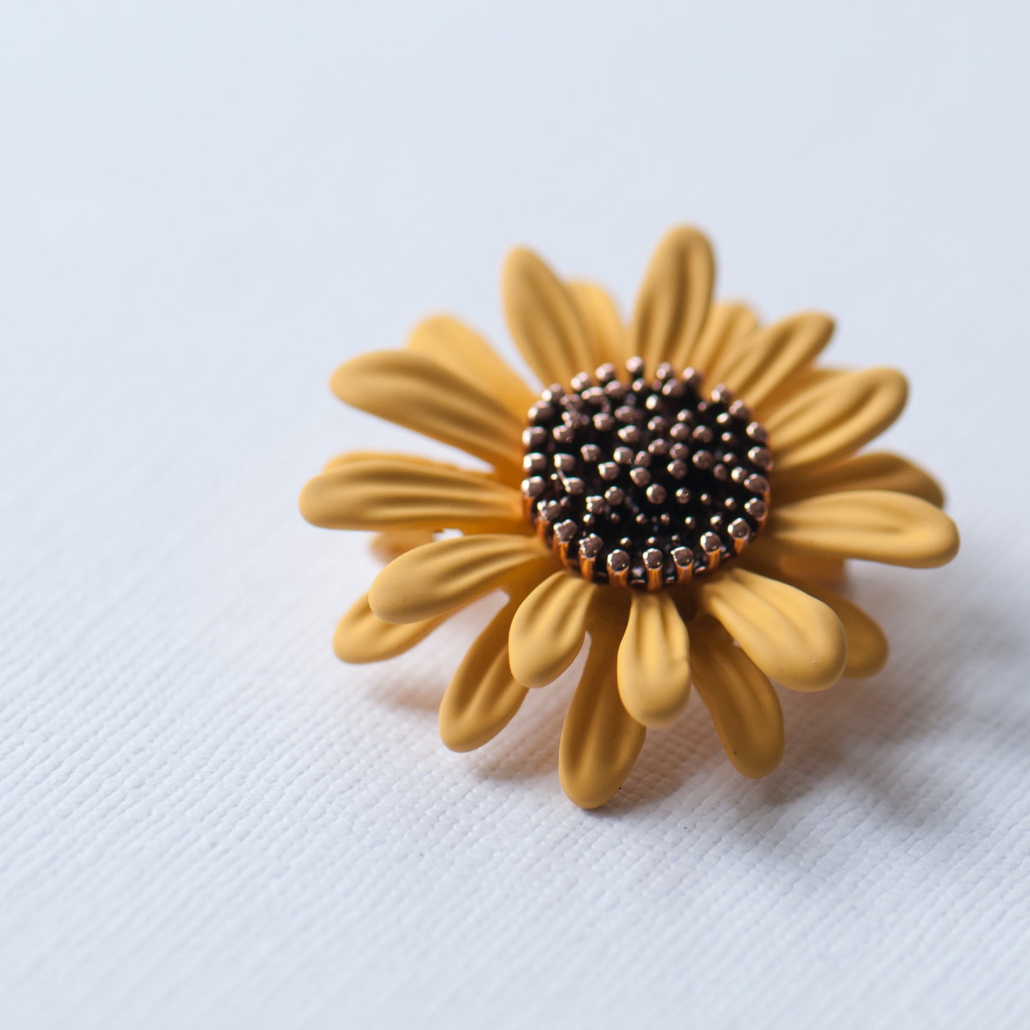 Yellow sunflower-shaped brooch with a black and gold center on a white background