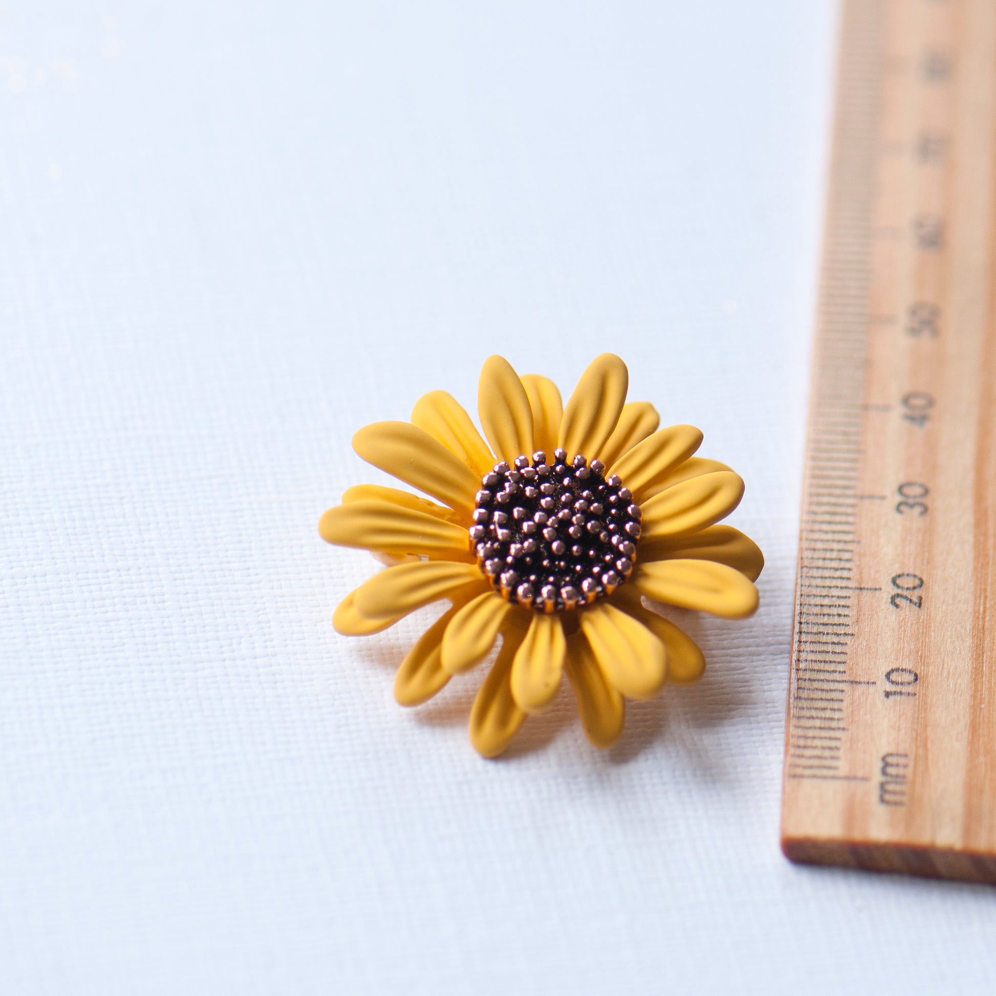 Yellow sunflower-shaped object next to a wooden ruler on a white background