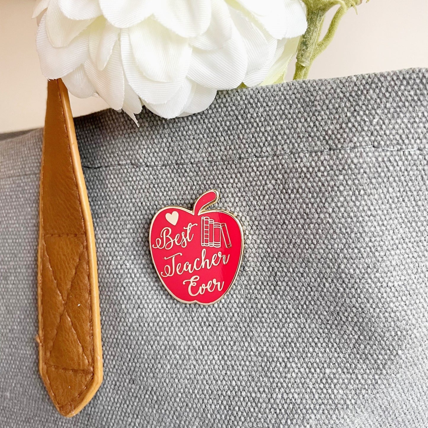 Red apple-shaped pin with 'Best Teacher Ever' text on a gray bag