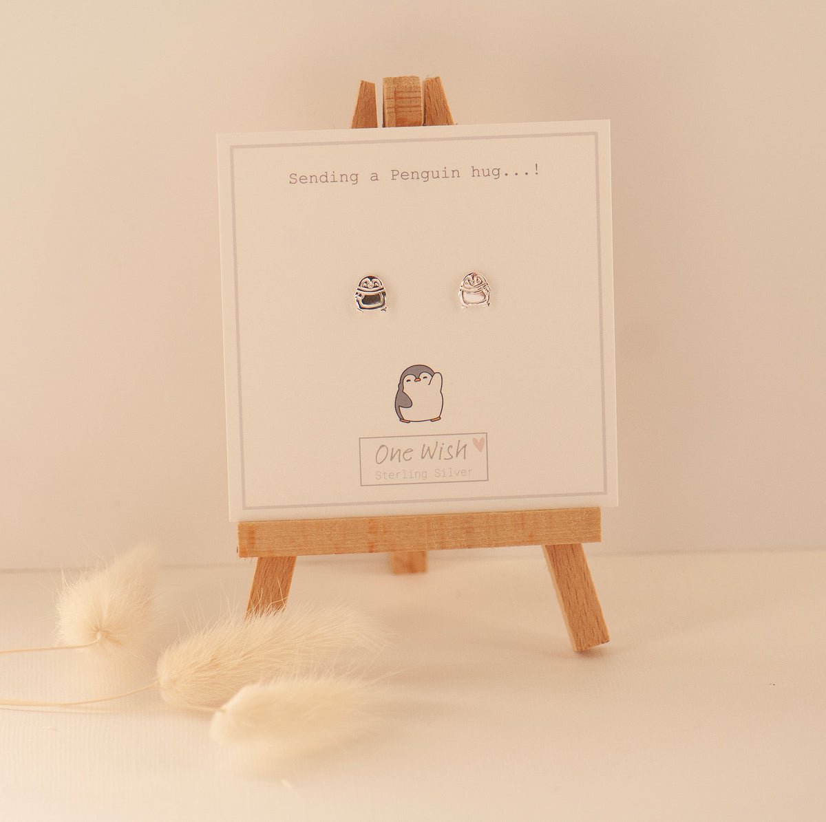 sterling silver penguin stud earrings on a gift card on an easel and the gift card says 'sending penguin hugs'
