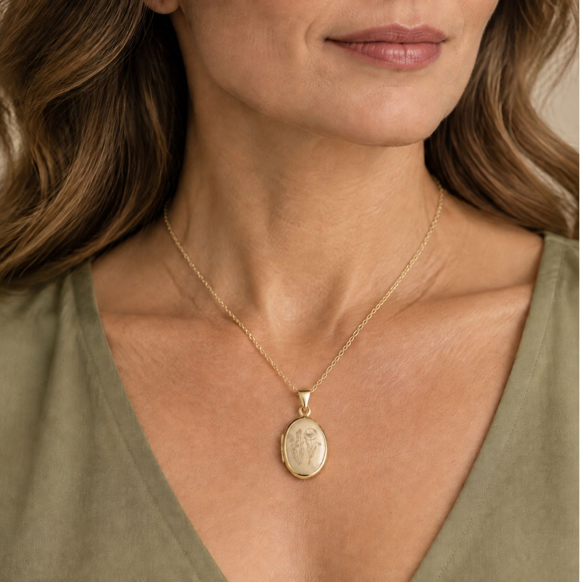 A close-up of a woman wearing a delicate silver chain necklace with an oval pendant featuring two engraved birth flowers