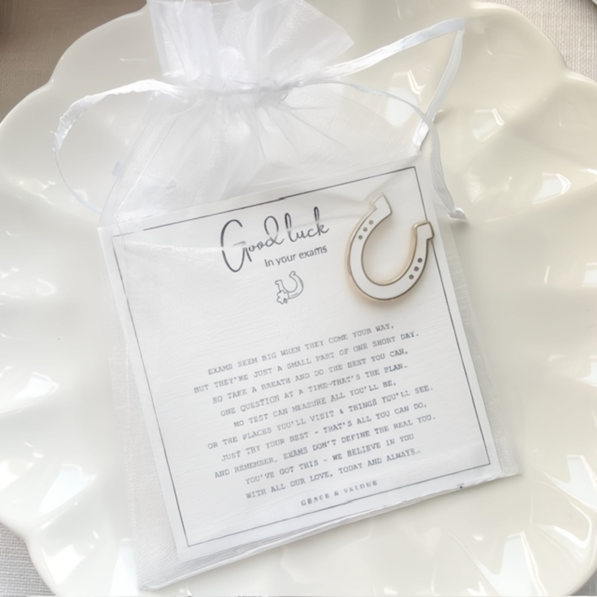 White drawstring bag with a horseshoe enamel pin and a  gift card inside on a white background